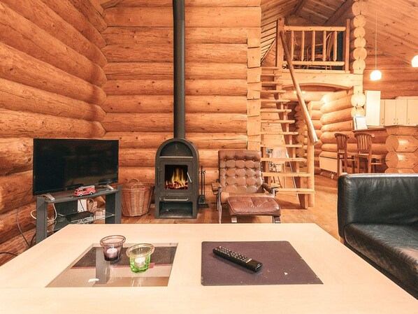A log cabin interior with a fireplace, a television, a sofa, and a dining area.