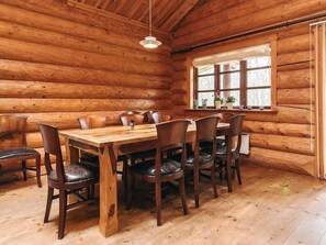 A wooden cabin interior with a dining table, chairs, and a window with curtains. - 5 Star Holiday Home in Hadsund (Hadsund)