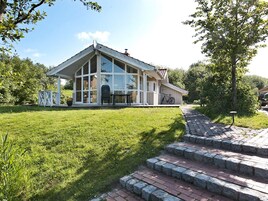 A house with a large glass front, a covered porch, and a brick pathway leading to the entrance.