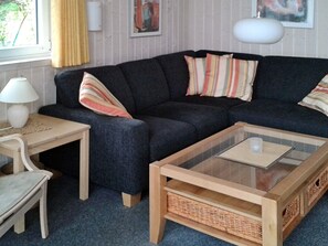 A living room with a dark sofa, striped pillows, a glass-top coffee table, a wooden side table, and a chair.