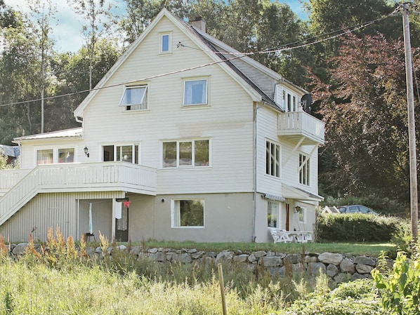 A two-story house with a balcony, a stone wall in front, and a car parked nearby.