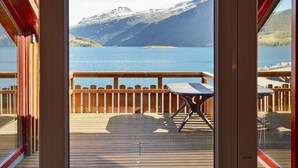Une terrasse en bois avec une table et des chaises, donnant sur un lac et des montagnes.