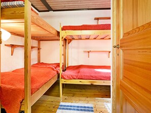 A bunk bed room with wooden walls and floors, a red blanket on one bed, and a blue and white striped rug on the floor. - 4 Person Holiday Home in Monsteras (Monsteras)