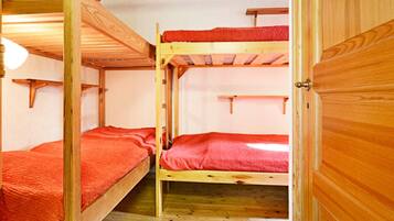 A bunk bed room with wooden walls and floors, a red blanket on one bed, and a blue and white striped rug on the floor.