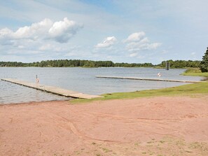 A lakeside area with two docks extending into the water, surrounded by grassy banks and a forested shoreline. - 4 Person Holiday Home in Monsteras (Monsteras)