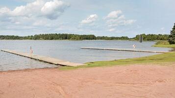 A lakeside area with two docks extending into the water, surrounded by grassy banks and a forested shoreline.