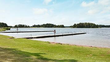 A calm lake with a grassy area in the foreground and a dock extending into the water.