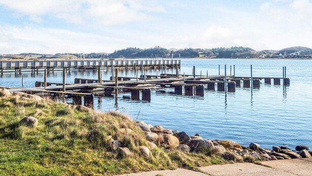 A waterfront dock with multiple piers extending into calm water, surrounded by grassy areas and distant hills. - 12 Person Holiday Home in Hojslev-by Traum (Hojslev)