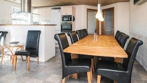 A spacious dining area with a long wooden table and black leather chairs, a kitchen with modern appliances, and a wooden ceiling. - 12 Person Holiday Home in Hojslev-by Traum (Hojslev)