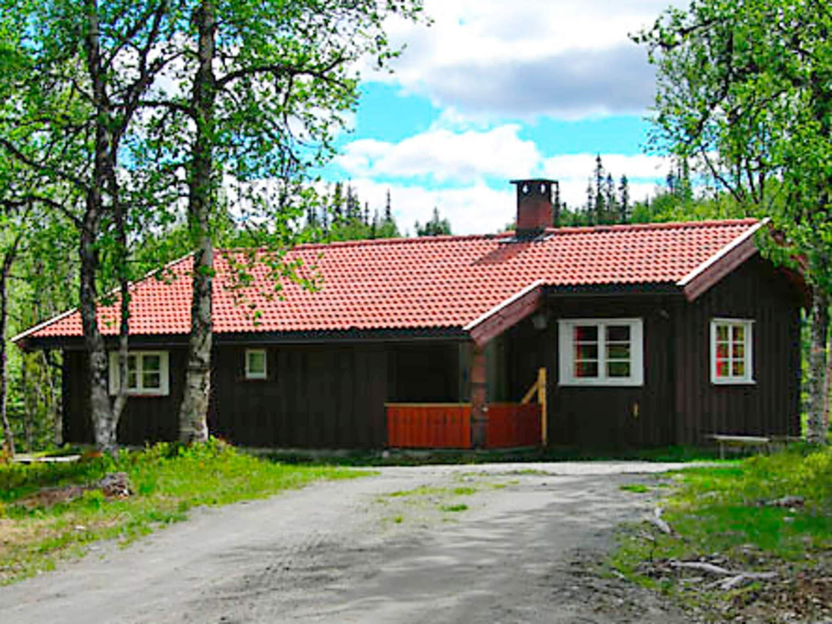 Une cabane rustique en bois, avec un toit recouvert de tuiles rouges, une cheminée et un porche en bois.