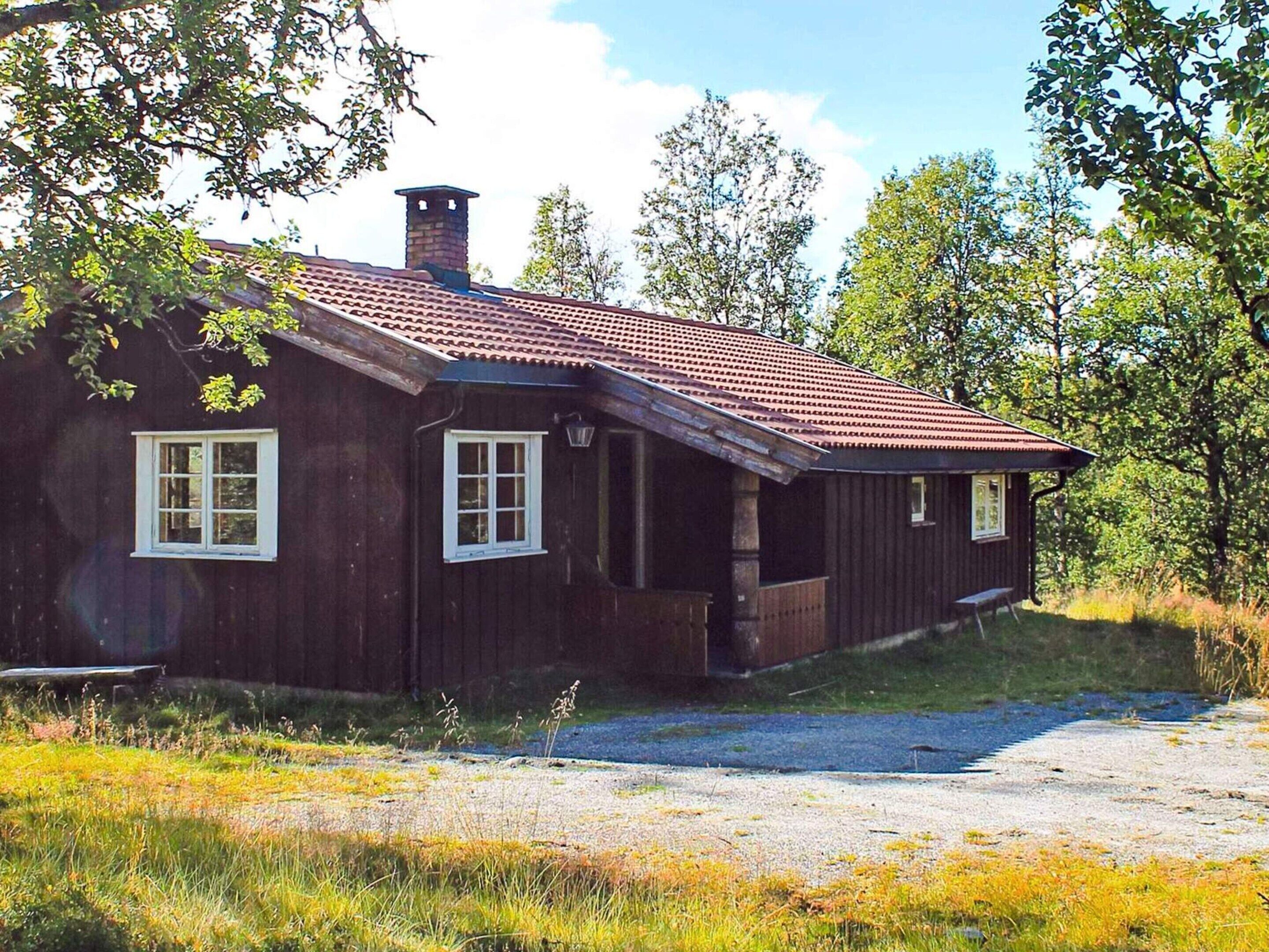 Une cabane en bois rustique, avec un toit recouvert de tuiles rouges, une cheminée et une allée gravillonnée.