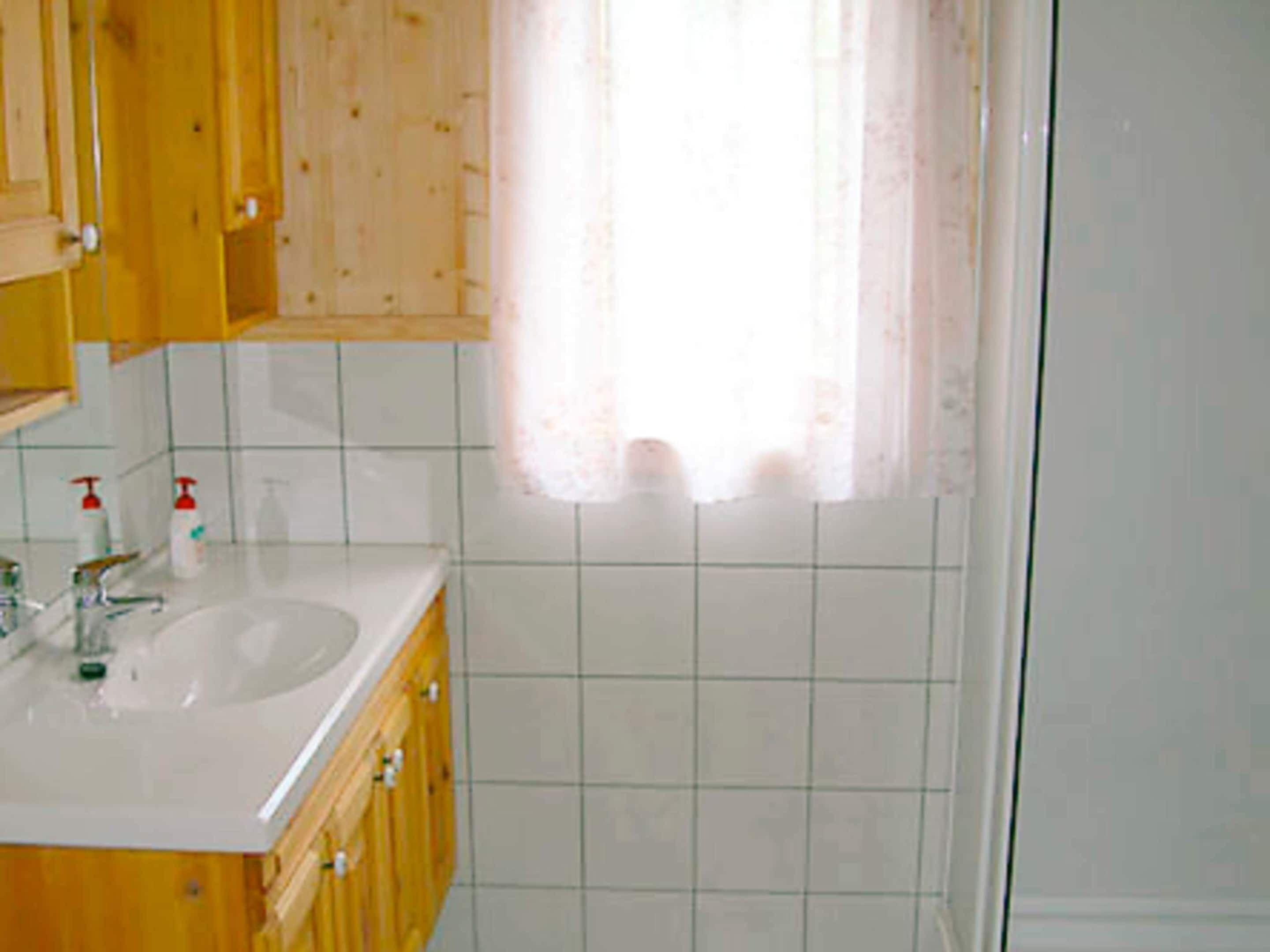 A bathroom with wooden cabinets, a white sink, and a window with a curtain.