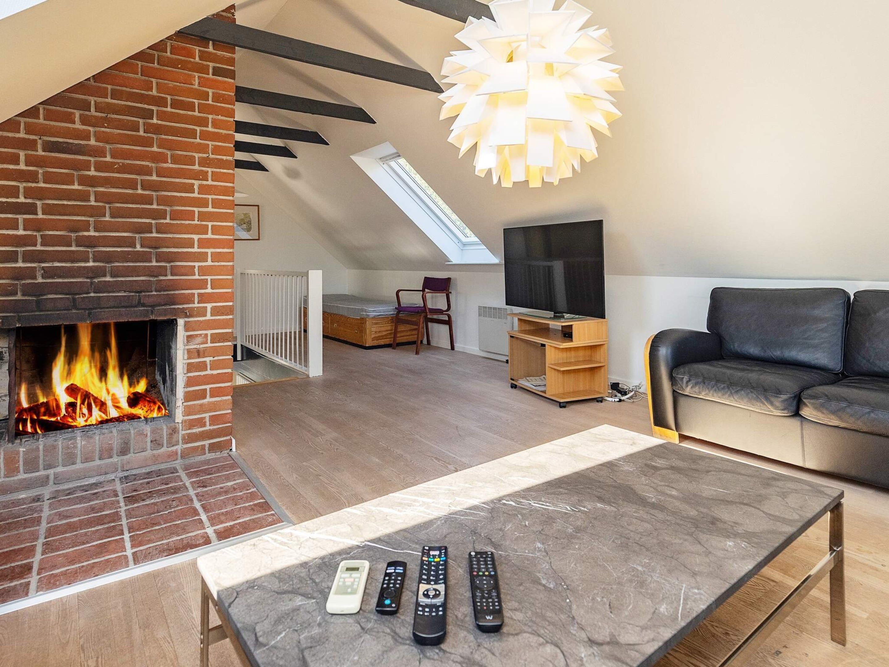 A living room with a brick fireplace, a sofa, a coffee table with remotes, and a TV on a stand.