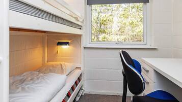 A bunk bed with a desk and chair, a window with a view of trees, and a wall-mounted heater.