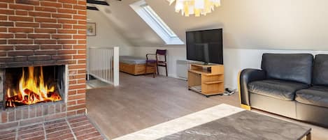 A living room with a fireplace, a sofa, a coffee table with remotes, and a TV stand.