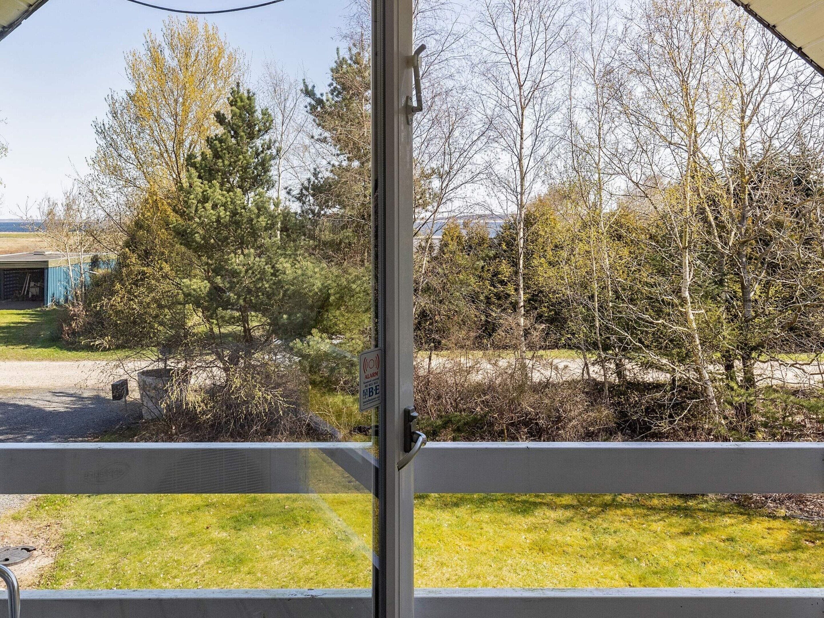 A view through a window with a metal frame, a grassy area, and trees in the background.