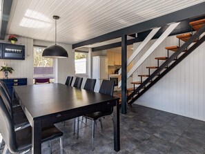 A modern kitchen with a central island, a dining area with a long table and chairs, and a staircase with wooden steps.