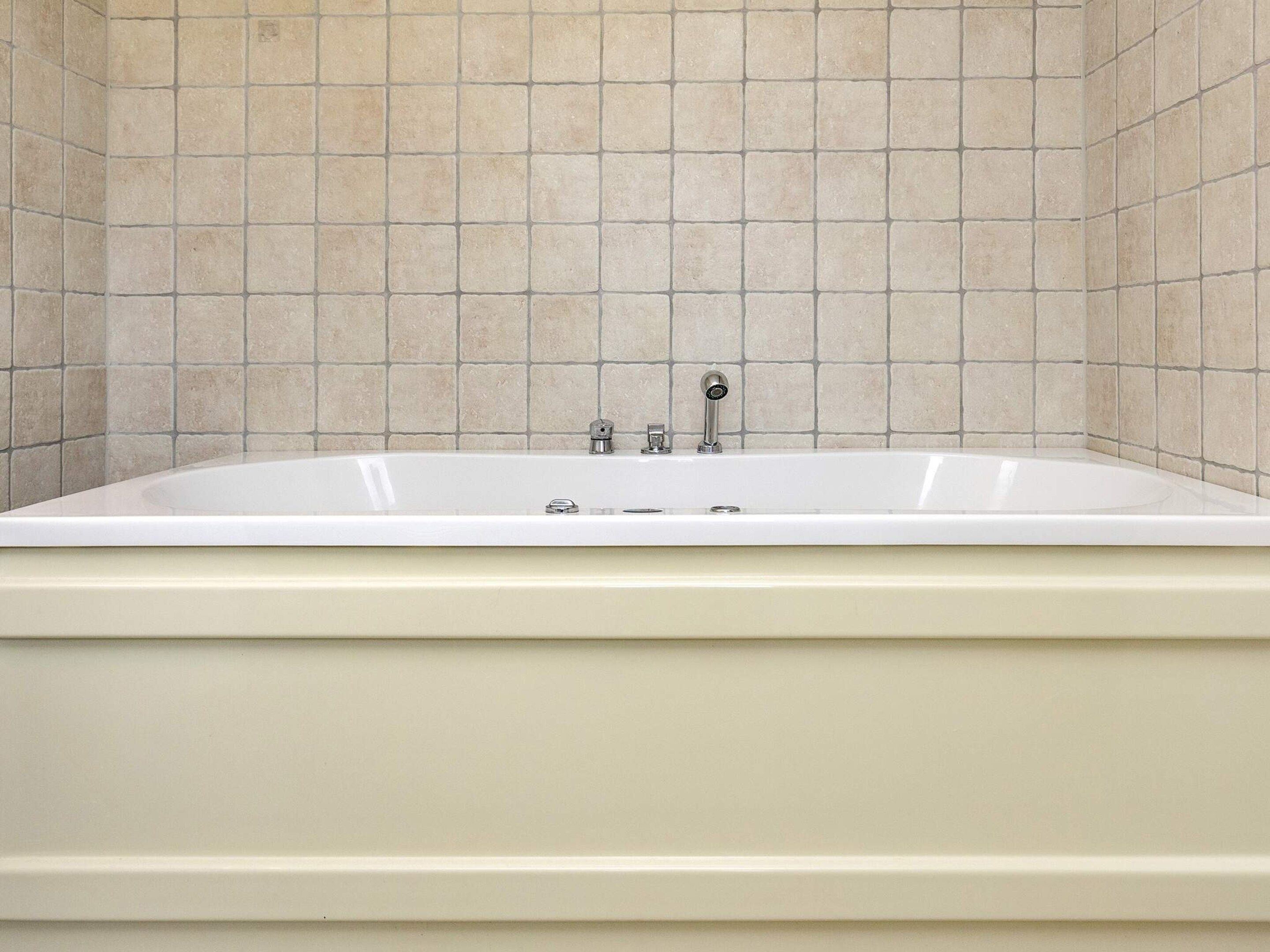 A standard bathtub in a bathroom with tiled walls.