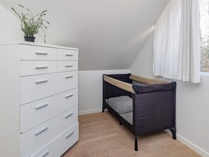 Una habitació amb una llitera, una petita còmoda blanca amb calaixos múltiples i una finestra amb cortines.