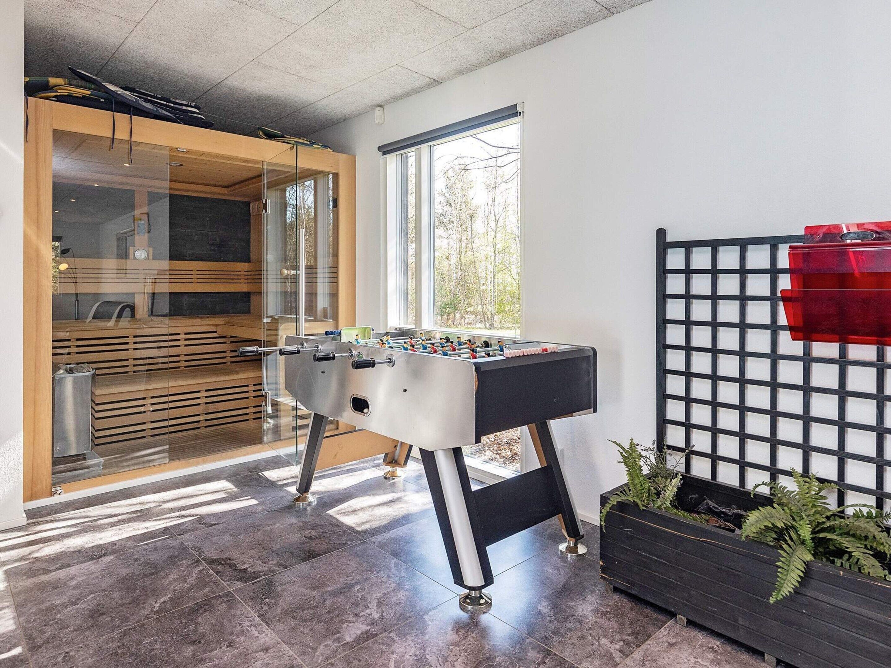 A room with a foosball table, a window with a view of trees, and a red object on a black grid structure.