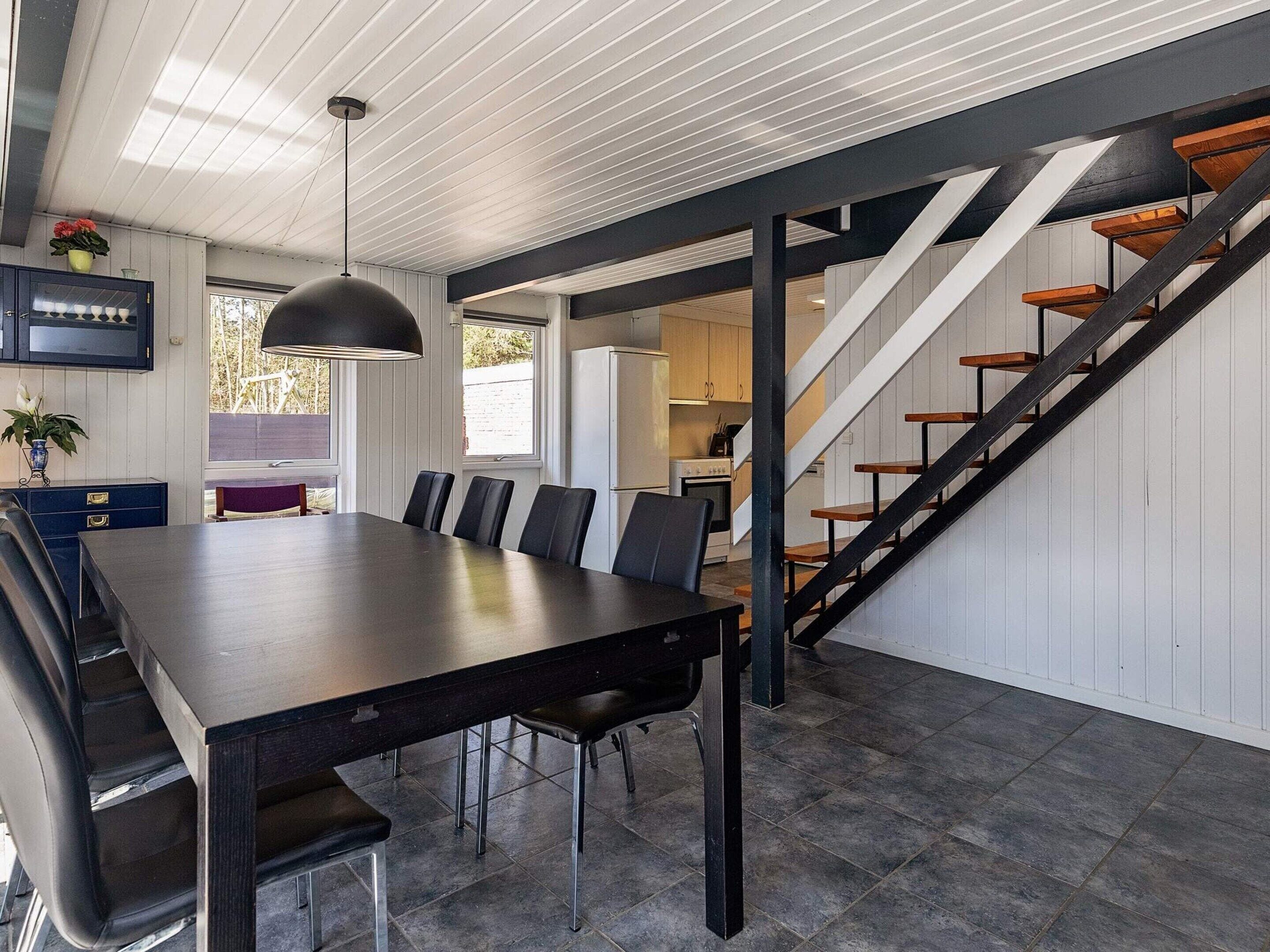A modern kitchen with a built-in oven, a dining area with a long table and chairs, and a staircase with wooden steps.