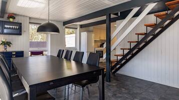 A modern kitchen with a built-in oven, a dining area with a long table and chairs, and a staircase with wooden steps.
