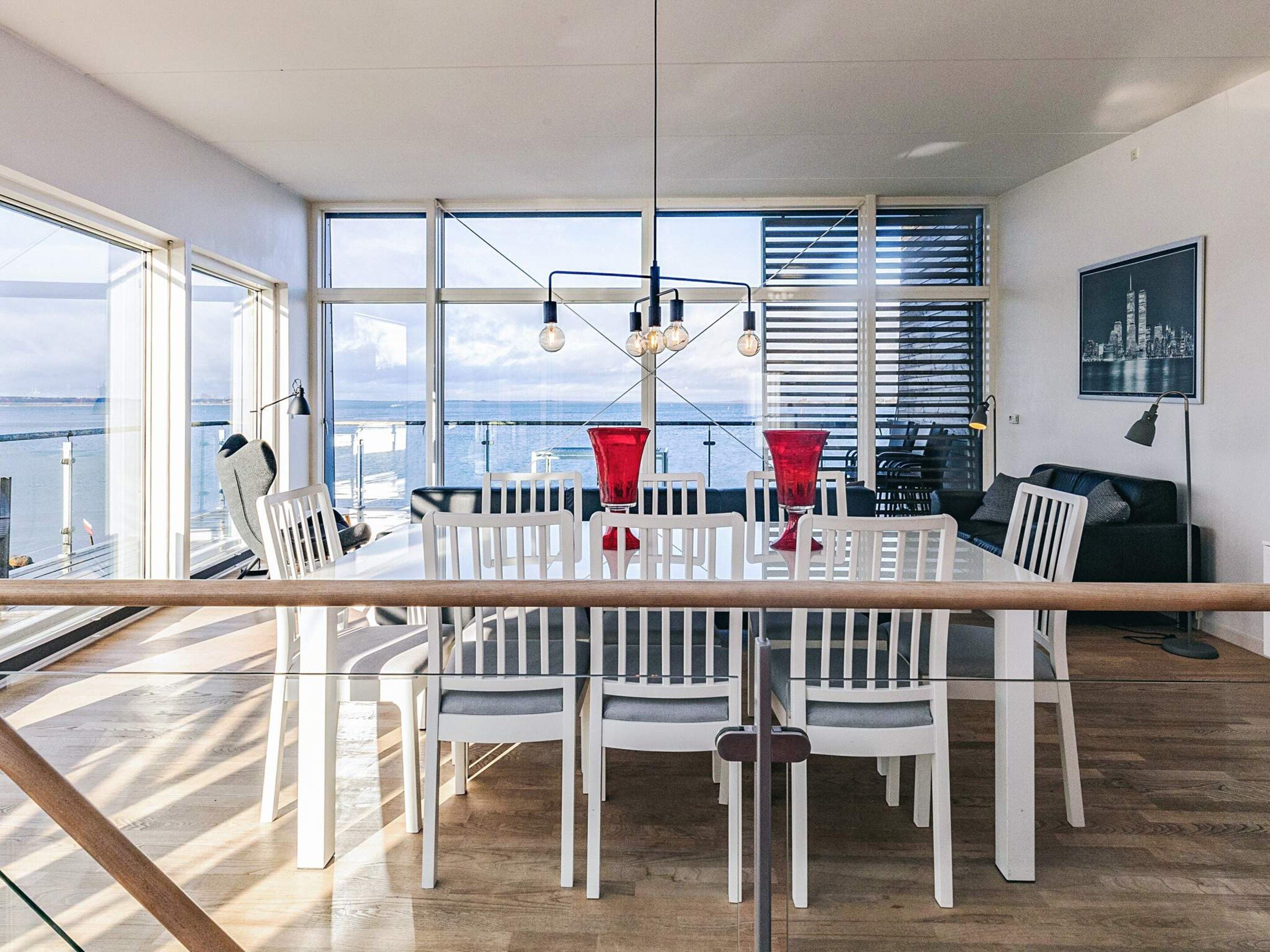Un espace repas moderne avec une table en verre, des chaises blanches et des vases rouges.
