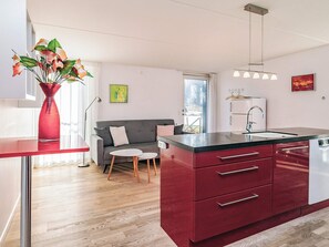 Una cucina moderna con un'isola rossa, un divano grigio e un vaso con fiori.