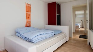 A modern bedroom with a white bed, a red cabinet, and a wooden floor.