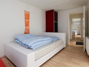 Een moderne slaapkamer met een wit bed, een rode kast en een houten vloer.