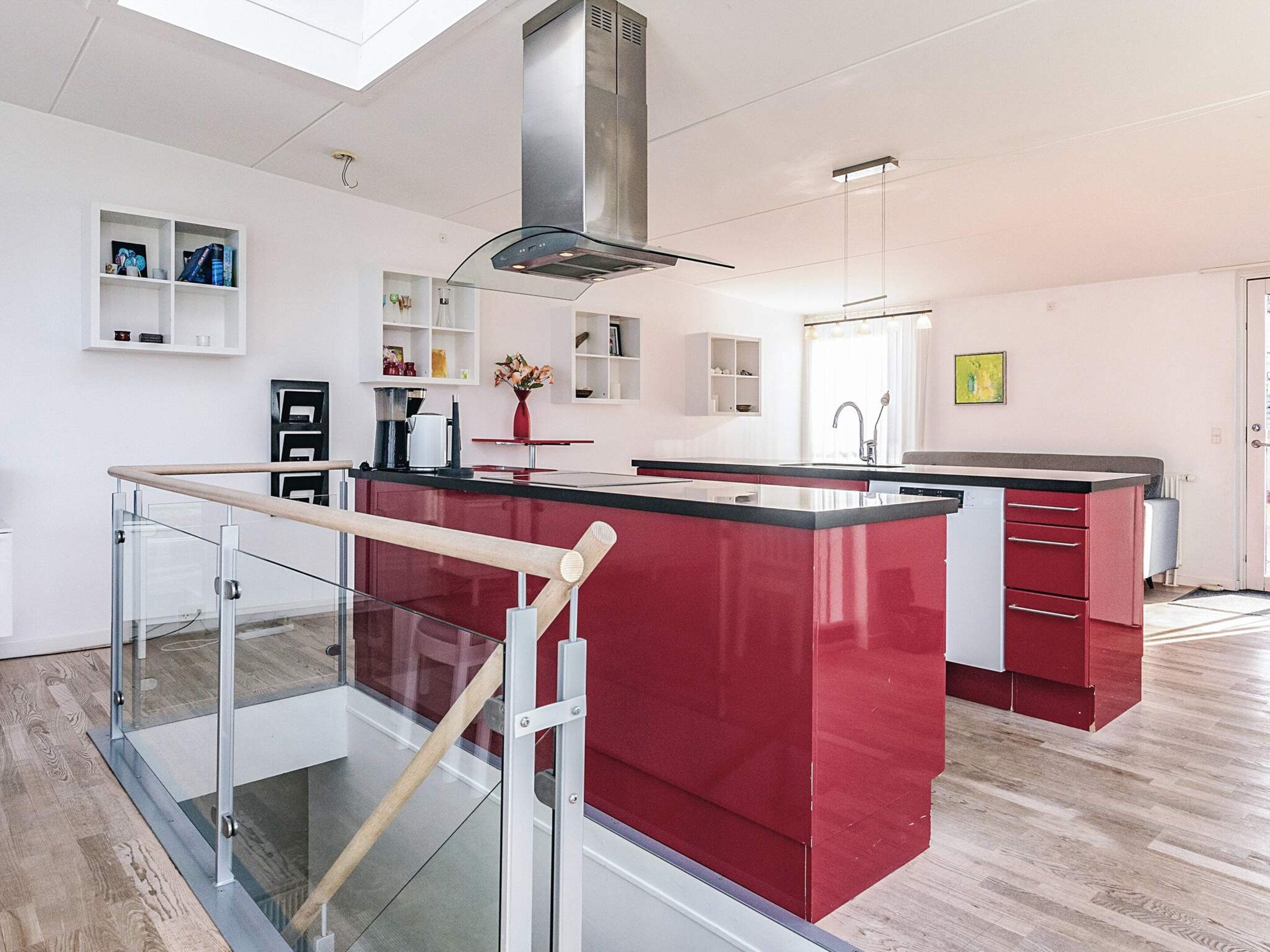 A modern kitchen with a central island, a glass railing, and a stainless steel range hood.