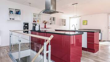 A modern kitchen with a central island, a glass railing, and a stainless steel range hood.