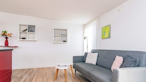 A modern living room with a grey sofa, white side tables, and a red accent piece.