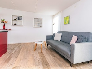 Een moderne woonkamer met een grijze bank, witte bijzettafels en een rode accentkleur.