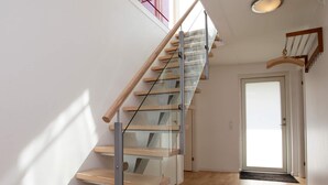 A modern staircase with glass railings and wooden steps leading to a door.