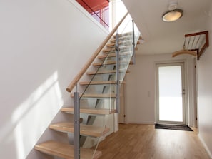Een moderne trap met glazen leuningen en houten treden die naar een deur leiden.