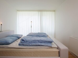 A bed with a mattress, pillows, and a bedside lamp in a room with a window and a radiator. - 7 Person Holiday Home in Stege (Stege)