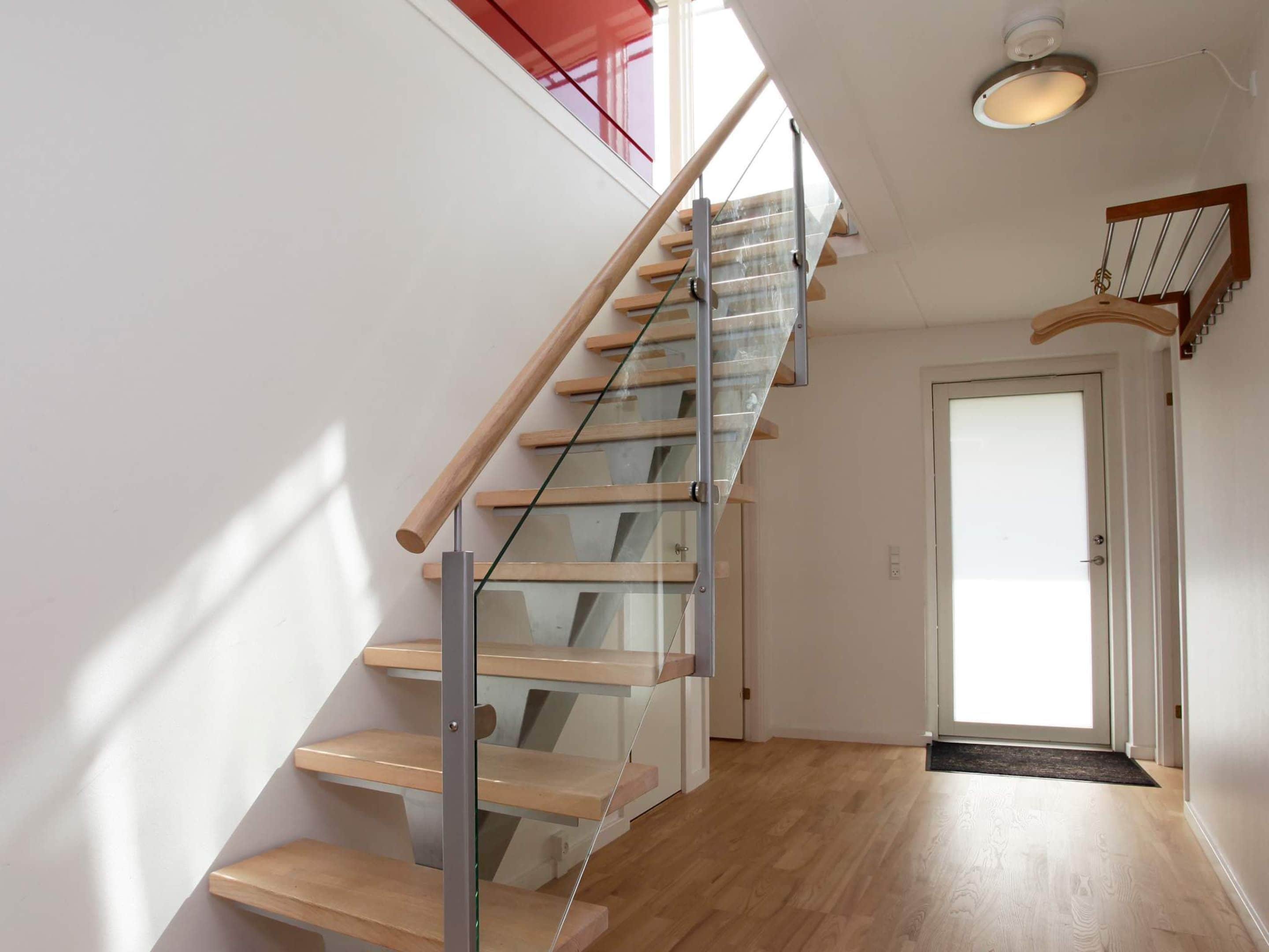 A modern staircase with glass railings and wooden steps leading to a door.