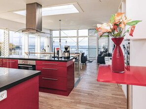 A modern kitchen with a large island, red cabinetry, and a view of the sea. - 7 Person Holiday Home in Stege (Stege)