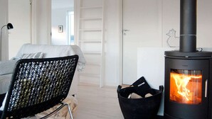 Habitació moderna amb un llit, una cadira de vimet negre, una estufa negra amb flames visibles i una porta blanca amb un dibuix d'una mascota.