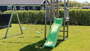 A wooden play structure with a slide and swings in a grassy yard. - Spacious Retreat With Whirlpool - By Traum Ferienwohnungen (Hadsund)