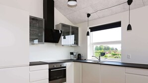 A modern kitchen with white cabinetry, a black countertop, and a window with a view of greenery. - Spacious Retreat With Whirlpool - By Traum Ferienwohnungen (Hadsund)