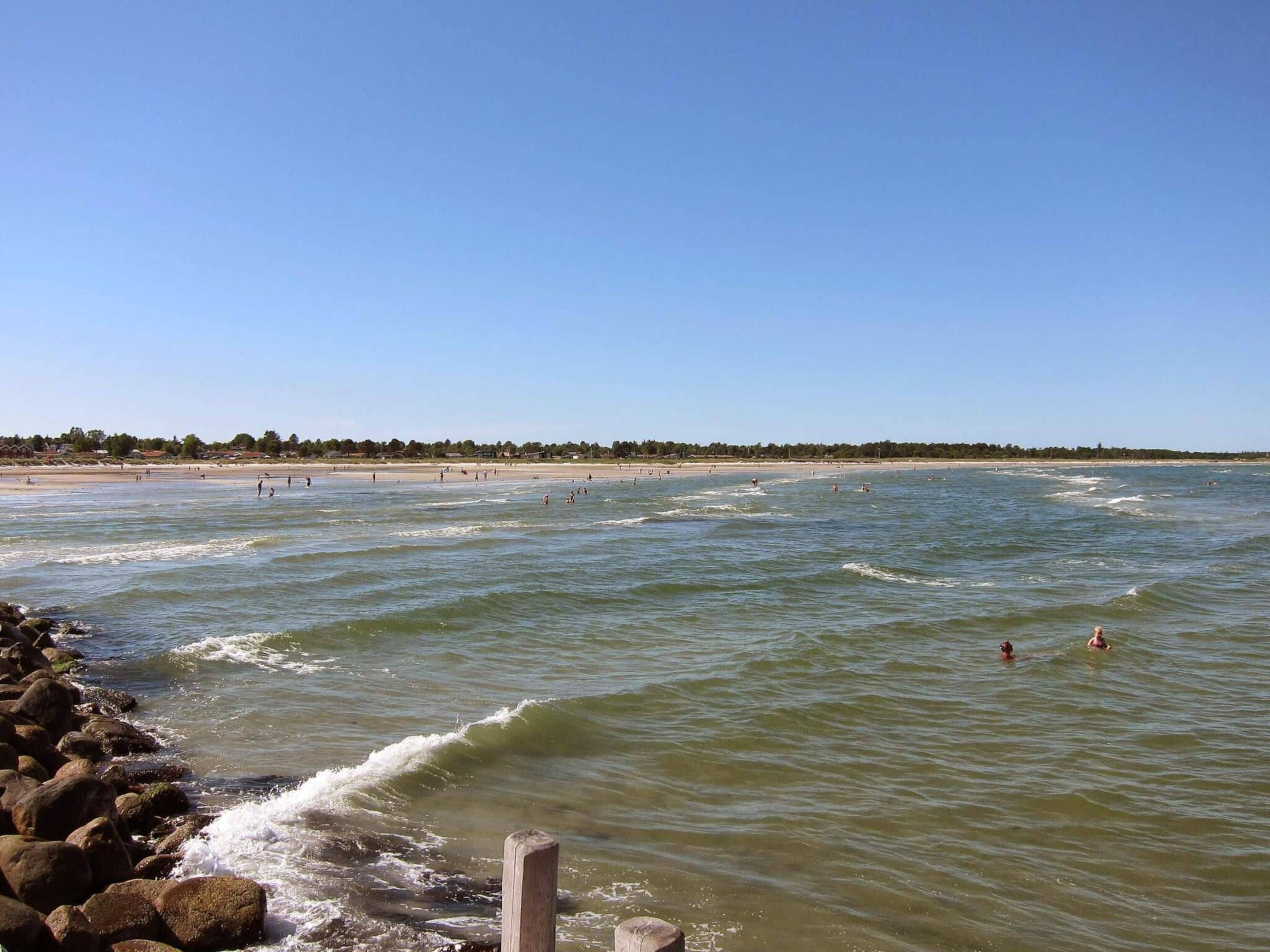 A beach with waves, a rocky shoreline, and a clear sky.
