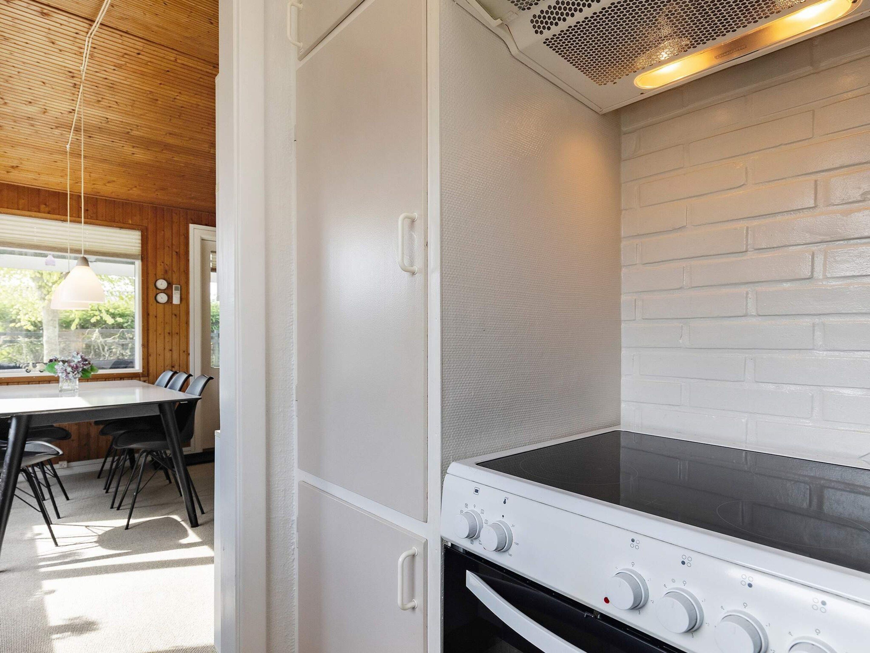 A kitchen with a white brick wall, a stove with control knobs, and a dining area with a table and chairs.