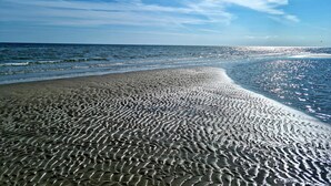 En strand med et mønstret sand og en klar himmel, samt havet i baggrunden.
