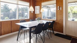 Et spiseområde med træloft, et bord med stole og store vinduer med persienner.