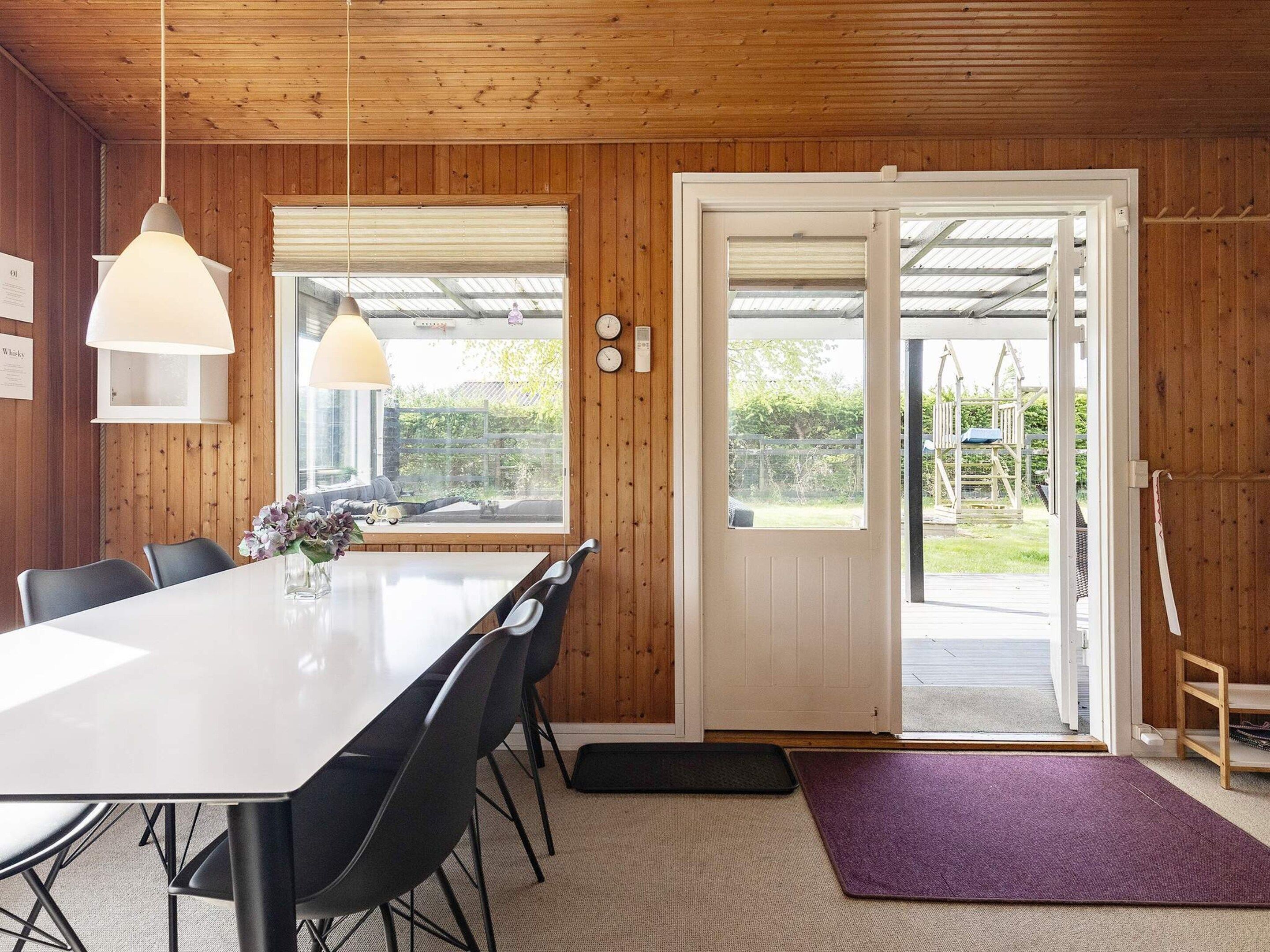 A dining area with a large table, chairs, pendant lights, and a view through a glass door to an outdoor space.