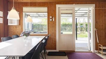 A dining area with a large table, chairs, pendant lights, and a view through a glass door to an outdoor space.