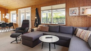 En moderne stue med en hjørnesofa, et rundt sofabord og et spiseområde med stole og bord.