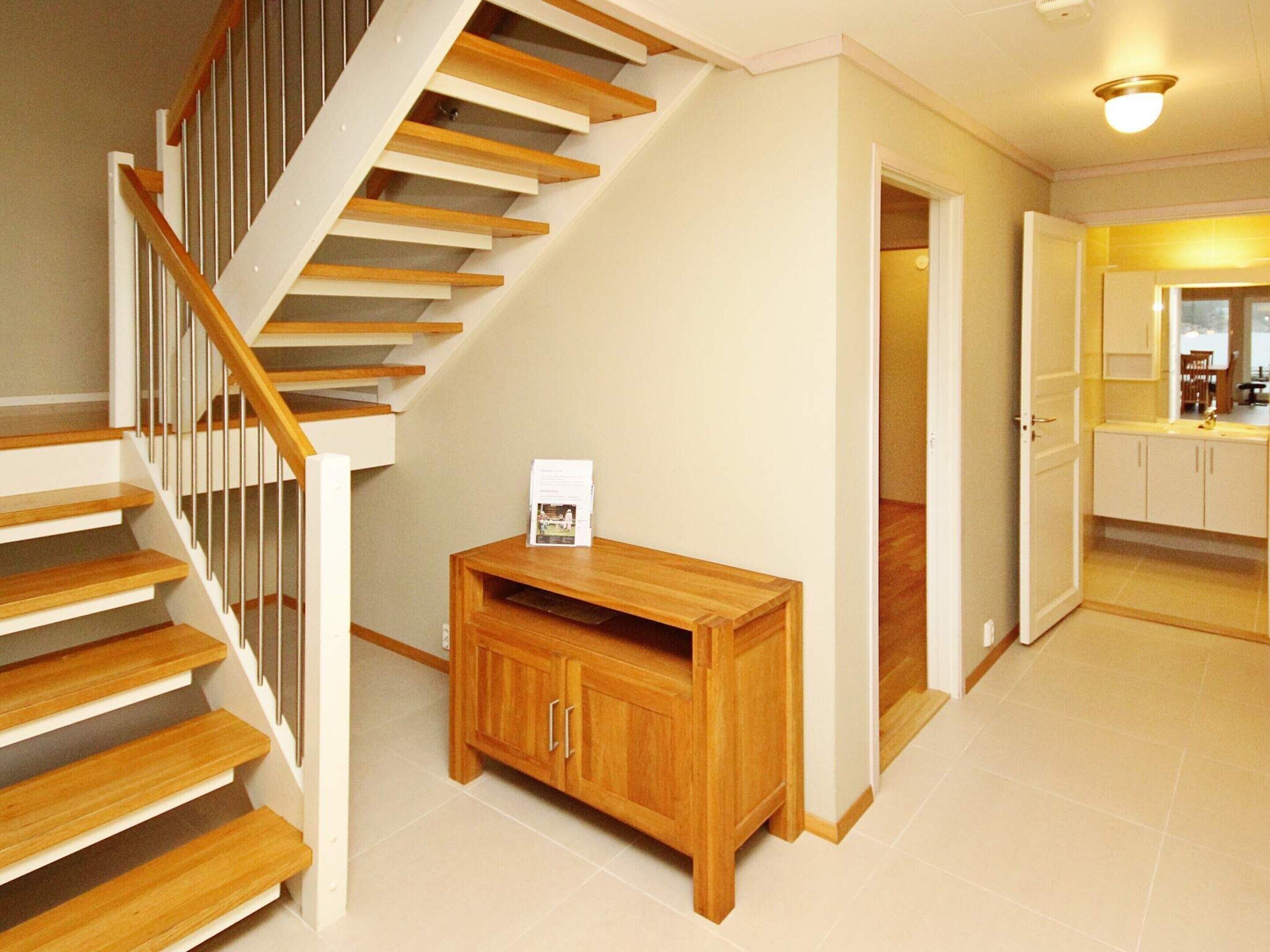 A staircase with wooden steps and white railings, leading to a kitchen area with white cabinets and a countertop.